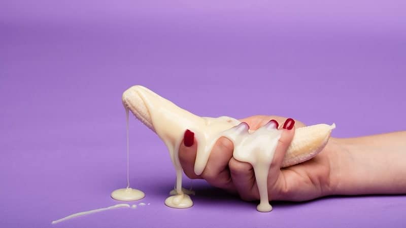 Banana (pênis) com leite condensado (ejaculação) em uma mão feminina