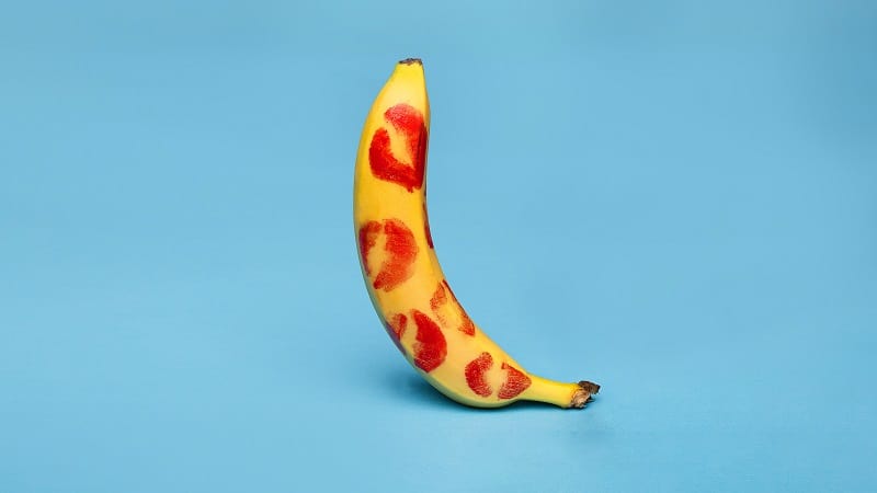 Banana em pé, ereta, repleta de marcas de beijos de batom ilustrando o tema "o que é ereção"