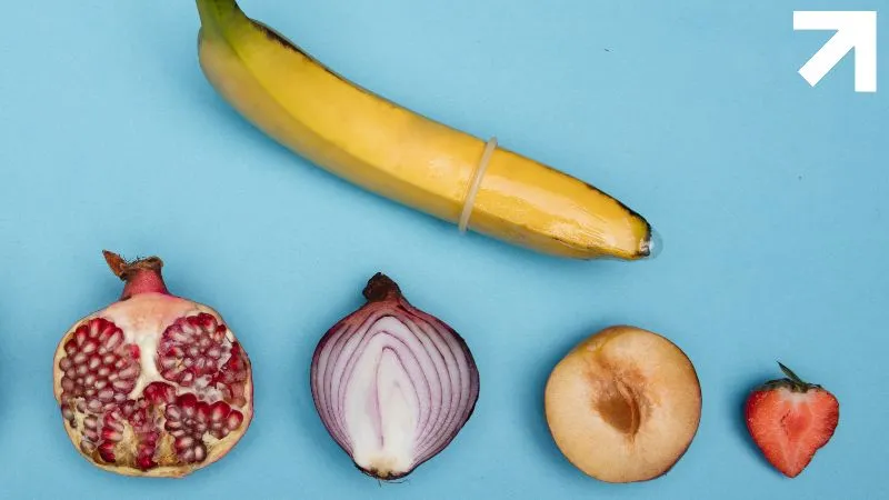 uma banana com preservativo, meio pêssego, meia cebola, vegetais imitando órgãos genitais